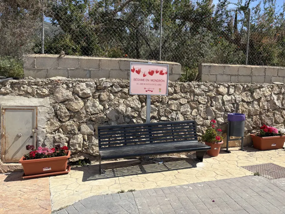 Banco con el cartel «Bésame en Mondrón» junto a un muro de piedra